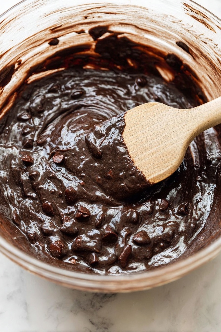 A close-up view of a dessert in a metal tray, showing a single thick layer mixed with melted caramel, dark chocolate chips, and chopped pecans scattered and partly melted on top, creating a sticky shiny texture with rough nut pieces spread evenly across the surface, all sitting on a white marbled background, photo taken with an iphone --ar 2:3 --v 7